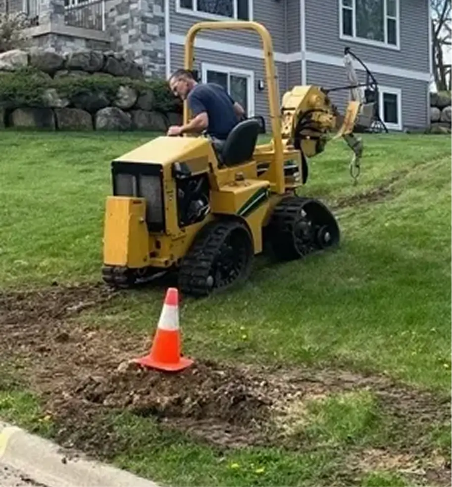 Man operating small trencher on grassy slope