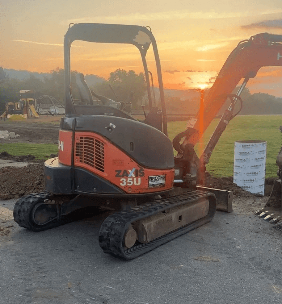 Mini excavator parked at sunset on a construction site.